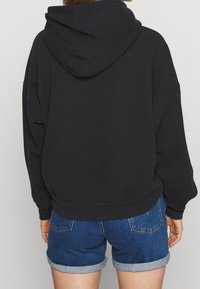 Sweat-shirt à capuche noir avec une coupe décontractée, des manches amples et une texture douce ; associé à un short en denim bleu avec des ourlets retroussés.