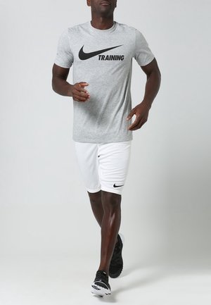 Nike träningsskjorta i grått med svart logga, matchad med vita shorts med en liten svart logga, bärs med svarta träningsskor.