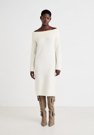 Off-shoulder krem strikket kjole med lange ermer, strukturert stoff, kne-lengde. Kombinert med beige thigh-high støvler med spenne detaljer.