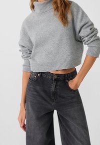 Pull gris court avec un col haut, des poignets et un ourlet côtelés, assorti à un jean noir taille haute à coupe décontractée avec des coutures visibles.