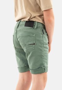 Pantalones cortos de algodón verde con puños enrollados, que cuentan con bolsillos traseros, una etiqueta de cuero negro y un detalle con cremallera en uno de los bolsillos.