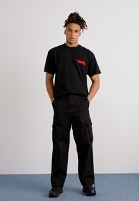 Schwarzes T-Shirt mit rographic, Cargo-Hosen und schwarzen Schuhen. Das Outfit hat eine lockere Passform und die Hose verfügt über Taschen.