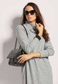 Grauer Pullover mit langen Ärmeln und Schalkragen; kombiniert mit einer schwarzen Lederhandtasche und übergroßen schwarzen Sonnenbrillen. Glatte Textur; elegantes Design.