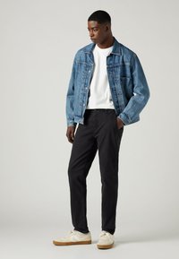 Denim jacket in light blue, white t-shirt, black pants, and cream shoes with gum sole. Simple design with classic fit, no notable patterns.