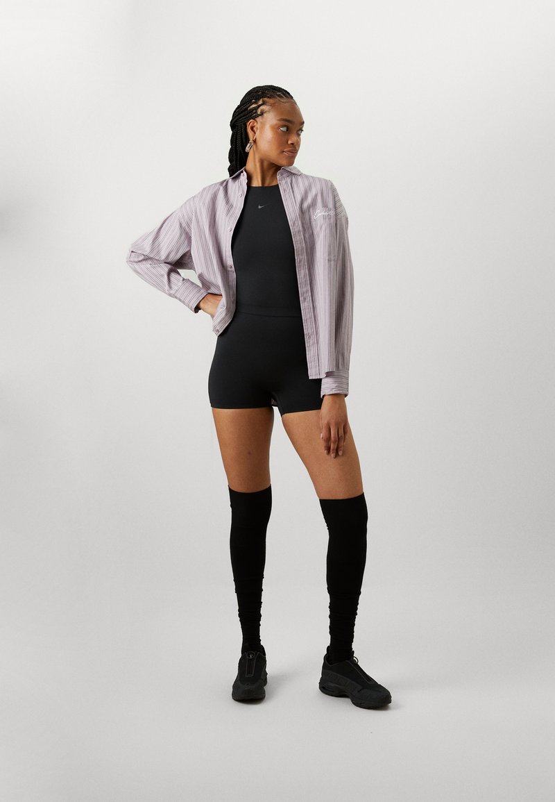 Body negro combinado con una camiseta de manga larga a rayas en púrpura claro, medias negras hasta la rodilla y zapatillas negras con textura.