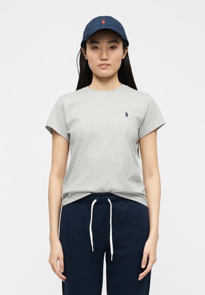 Γυναίκα που φοράει γκρι κοντομάνικο μπλουζάκι, σκουρόχρωμο μπλε φόρμα με λευκούς κορδόνια και σκουρόχρωμο μπλε καπέλο μπέιζμπολ.