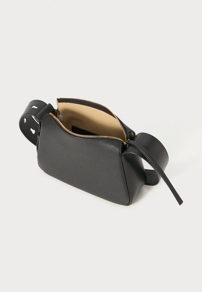 Sac en cuir noir en bandoulière avec une surface texturée, de forme triangulaire, fermeture éclair, et une sangle lisse avec des découpes.