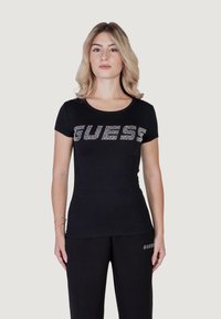 Musthave mustaga t-särk lühikeste varrukatega, millel on rinnas "GUESS" rhinestone'idega, sile kangas ja ümmargune kaelus.