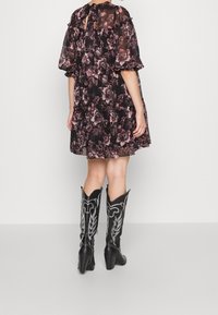 Robe noire à motifs floraux avec des manches bouffantes et des couches froncées ; portée avec des bottes de cowboy noires ornées de broderies argentées et à bouts pointus.