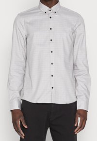 Camicia button-up grigia chiara con un sottile motivo a quadretti, bottoni neri e colletto a punta. Maniche lunghe con polsini bottonati.
