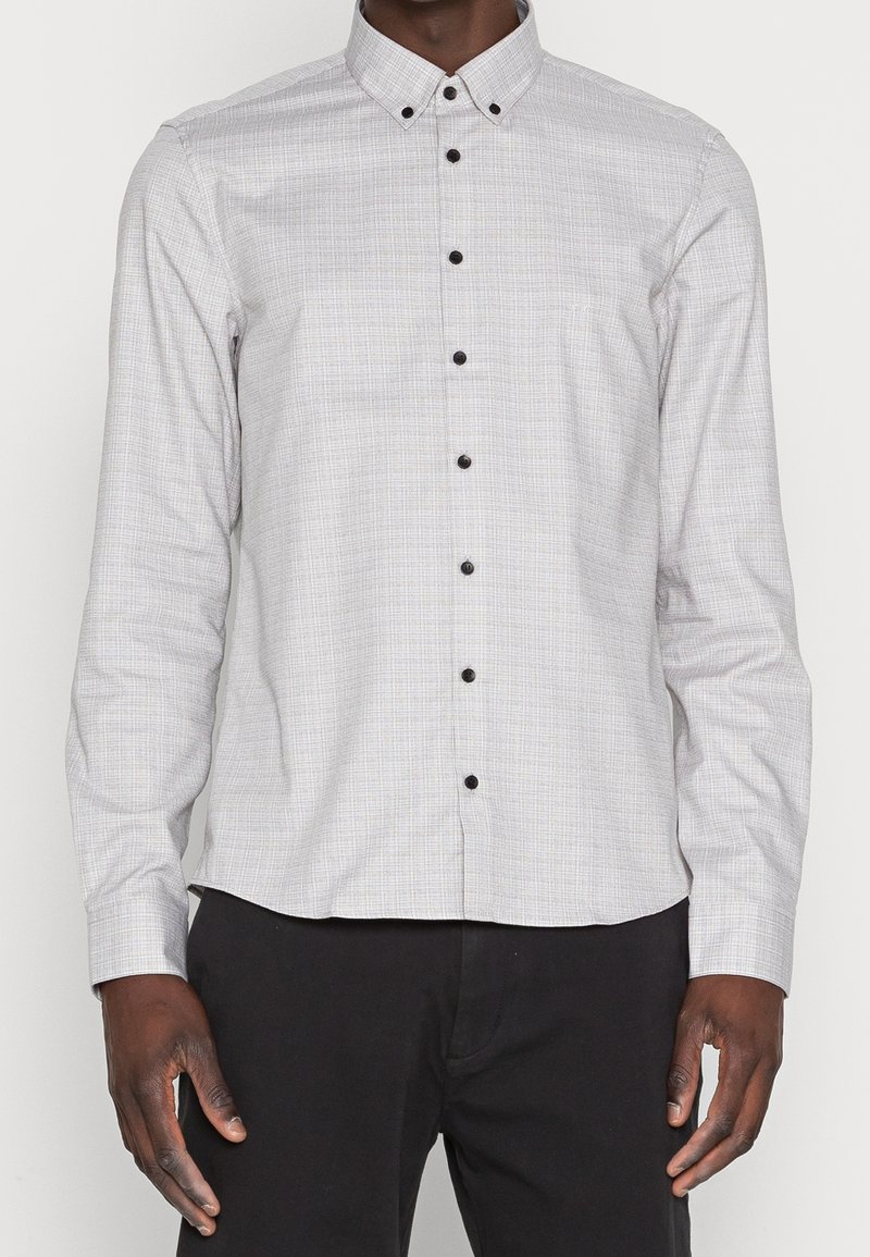 Camicia button-up grigia chiara con un sottile motivo a quadretti, bottoni neri e colletto a punta. Maniche lunghe con polsini bottonati.