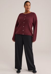 Burgundy stickad kavaj med långa ärmar, rund hals och pärlknappar. Matchad med svarta vida byxor och svarta sneakers.