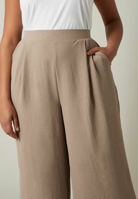 Beige wijde broek van textuurstof, met een hoge tailleband en zijzakken. Soepele, ontspannen pasvorm met een natuurlijke val.
