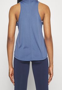 Débardeur de sport bleu avec un dos nageur, fabriqué en tissu respirant, doté de coutures plates et d'un ourlet incurvé pour le confort.