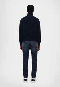 Marinefarbener Rollkragenpullover, taillierte Passform, weiche Textur. Kombiniert mit schmal geschnittenen, dunklen Jeans und weißen Turnschuhen mit schwarzen Akzenten.