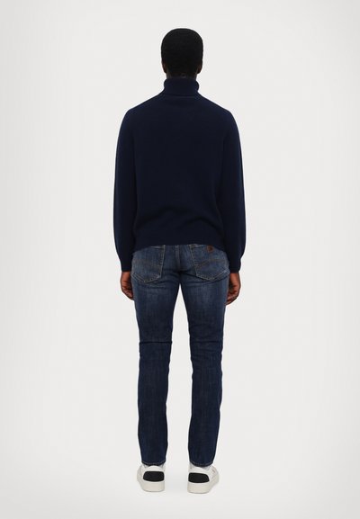 Navy turtleneck sweater, fitted design, soft texture. Paired with slim-fit dark denim jeans and white sneakers with black accents.