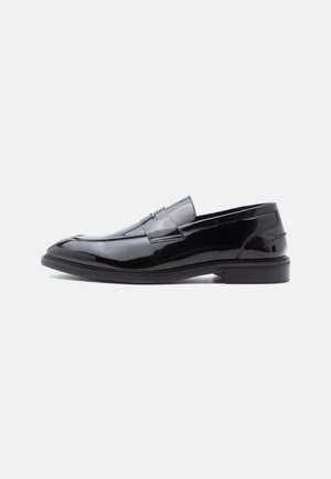 Black patent leather loafers with a smooth finish, rounded toe, and decorative strap detail, featuring a low profile and rubber sole.