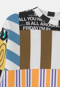 Pull en coton multicolore présentant un mélange de motifs audacieux, y compris des rayures, du texte et des formes géométriques dans des tons de bleu, marron, orange et blanc.