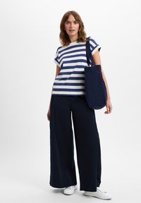 Gestreept katoenen T-shirt in marineblauw en wit, gecombineerd met wijde marineblauwe broeken en een bijpassende tote bag. Witte sneakers maken de outfit compleet.