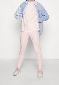 Růžové sportovní kalhoty a odpovídající tričko navlečené pod modro-bílou pruhovanou košilí. Oblečení obsahuje loga Nike a pastelové barvy.