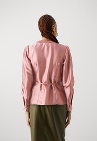 Rosa gestreiftes Satinbluse mit einem Kragen aus Spitze, langen Ärmeln und einer taillierten Taille, kombiniert mit einem grünen Rock. Glatte Textur.