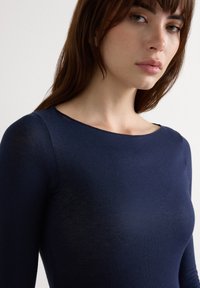 Granatowa bluzka z długim rękawem wykonana z lekkiego materiału; ma okrągły dekolt i gładką fakturę, podkreślającą kontury ciała.