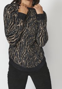 Suéter de punto con un patrón de rayas de cebra en azul marino y beige, cuello redondo y puños acanalados. Textura suave y dobladillo ligeramente curvado.