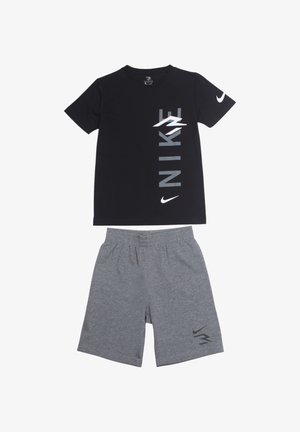 T-shirt noir Nike avec un logo vertical gris ; associé à un short de sport gris avec un logo noir sur le côté. Matière en coton.