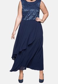 Robe bleu marine avec un corsage en dentelle florale et une jupe fluide et superposée. Le tissu est doux, avec une coupe à mi-genoux et une asymétrie subtile.