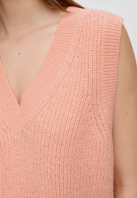 Rosa gestrickter ärmelloser Pullover mit tiefem V-Ausschnitt, gerippter Textur und subtilen vertikalen Details auf dem Stoff.