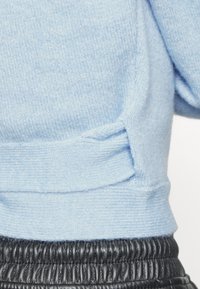 Jasnoniebieski sweter z dzianiny o teksturowym wykończeniu i wiązanym akcentem u dołu, zestawiony z czarnymi spodniami z plisowaną talią.