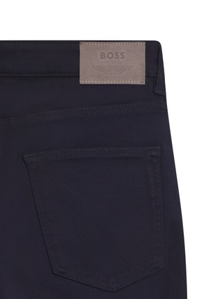 Pantaloni in tessuto blu navy con tasca posteriore e una toppa rettangolare in pelle con l'etichetta "BOSS" e un logo alato in rilievo. Texture liscia e cuciture pulite.