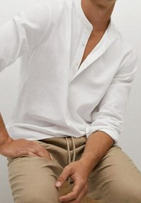 Witte linnen shirt met een mandarinekraag en drie knopen, gecombineerd met beige broek met trekkoord, met een losse pasvorm en gestructureerde stof.