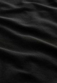 Gros plan d'un tissu noir lisse avec des plis doux et fluides et une texture subtile visible sous un éclairage doux.