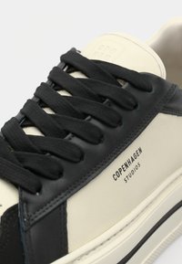 Baskets en cuir crème et noir avec lacets noirs, coutures visibles et inscription « Copenhagen Studios » sur le côté.