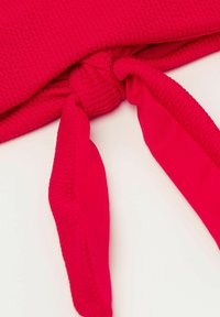 Topy z hot pink látky s texturovaným povrchem a designem s uzlem v přední části, doplněné dvěma dlouhými zavazovacími detaily. Hladký a elastický materiál.