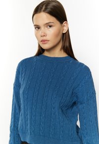 Maglione blu a maglia thomn assottigliato con scollatura rotonda, polsini e vita a coste. Presenta un motivo di maglia testurizzato e un design corto.