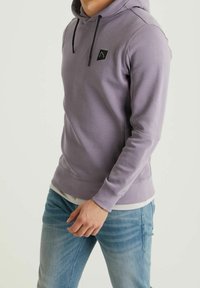Sudadera con capucha color púrpura claro en tela suave con un logo negro en el pecho, cuenta con capucha ajustable con cordón y puños y dobladillo acanalados.
