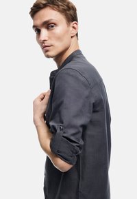 Donkergrijs overhemd met knopen, gemaakt van een zachte, licht gestructureerde stof. Heeft opgerolde mouwen, een kraag en een slim fit ontwerp.