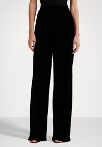 Pantalons larges noirs en velours lisse, taille haute et boucles de ceinture discrètes. Dotés d'une coupe classique et d'un design longueur totale.