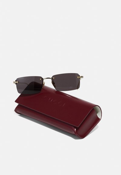 Ochelari de soare Gucci cu lentile închise la culoare și accente aurii pe cadrul negru, însoțiți de un toc din piele bordeaux cu un logo embosat.