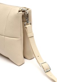 Beige leren schoudertas met een gestructureerd oppervlak, ritssluiting en verstelbare schouderband met een zilverkleurige metalen gesp.
