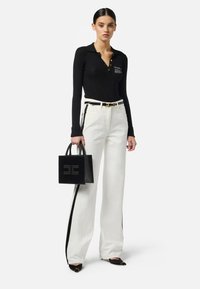 Top a maniche lunghe nero a coste con bottoni dorati, pantaloni bianchi a gamba larga con strisce nere laterali, borsa a tracolla nera con logo, scarpe nere con punta a punta.