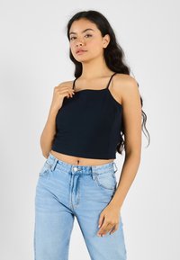 Mørkeblå, kort tanktop med tynne stropper, glatt tekstur, kombinert med lyseblå høytlivsjeans med knapp og glidelås.