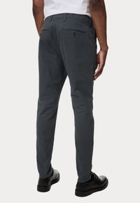 Grijze katoenen broek met een slim fit, met achterzakken, een gladde textuur en subtiele stikseldetails. Draagt een paar zwarte schoenen.