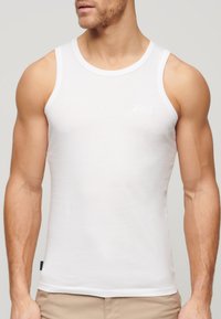 Top de algodón blanco sin mangas con un diseño ajustado. Cuenta con un escote redondeado y grandes aberturas para los brazos. Logo sutil impreso en el pecho.