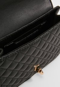 Borsa a tracolla in pelle trapuntata nera con hardware dorato. L'interno presenta più scomparti per carte e una fodera liscia. Forma rettangolare compatta.