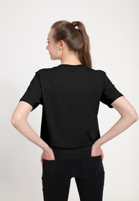 Černé tričko s krátkým rukávem vyrobené z bavlny, se kulatým výstřihem a volným střihem. Nenošené naopak, zdůrazňující hladkou texturu.