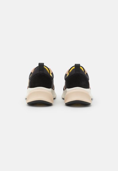 Sneakers med en svart mesh-överkropp, svarta detaljer i mocka, beige gummisula och en gul hältab. Unik design med kontrasterande material och texturer.