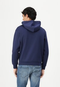 Navy blue hooded sweatshirt made of soft fabric, featuring long sleeves, a relaxed fit, and a ribbed hem, paired with light blue jeans.